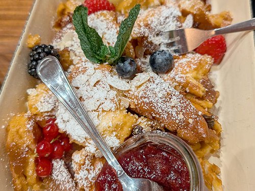 Kaiserschmarrn mit Puderzucker, Beeren und Preiselbeer-Kompott auf einem Teller.