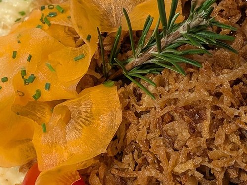 Nahaufnahme eines Tellers mit gebratenen Karottenscheiben, Röstzwiebeln und Rosmarin.