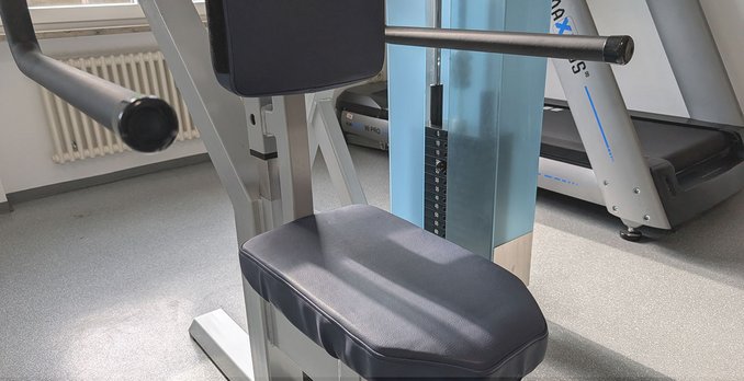 Nahaufnahme des Gewichtsgestells eines Trainingsgeräts, im Hintergrund ein Laufband.
